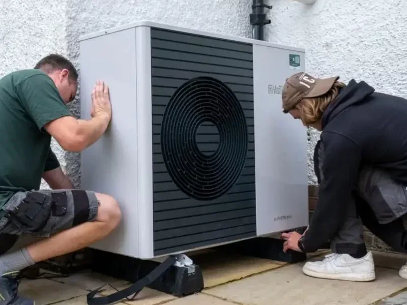 Engineers installing an air source heat pump outside a home
